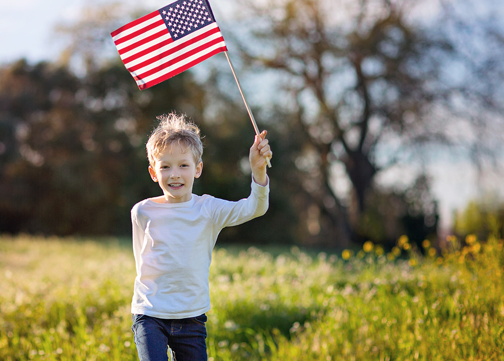Little Boy Holding American Flag and Walking Through Field