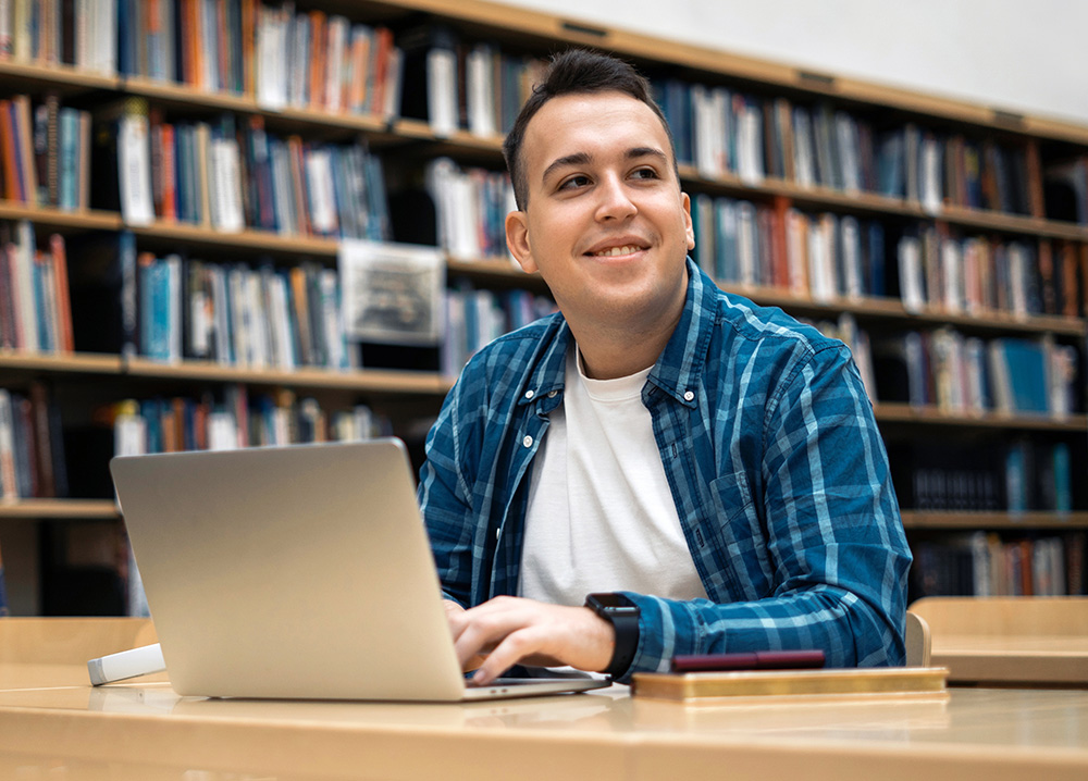 Happy Young Man on Laptop Computer in Library