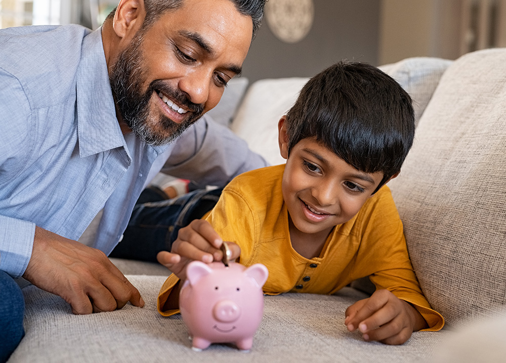 Indian Father and Son Putting Money into a Piggy Bank