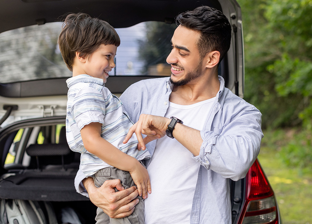 Father Holding Young Son Near Car